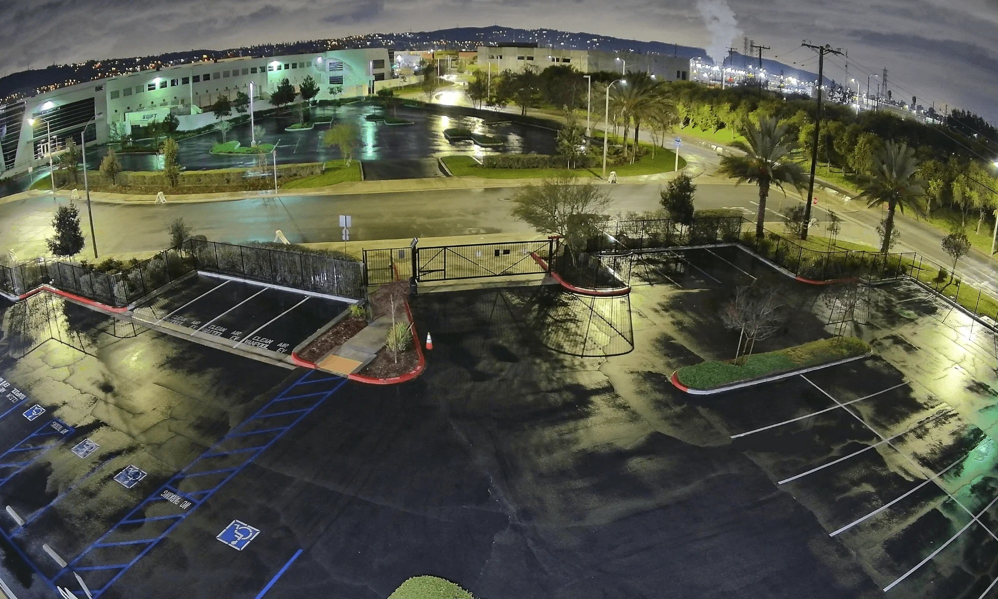 Glimpse the atmospheric scene of a sprawling parking lot at night, illuminated by streetlights, as seen from the vantage point of a panoramic security camera monitoring the area's tranquility.