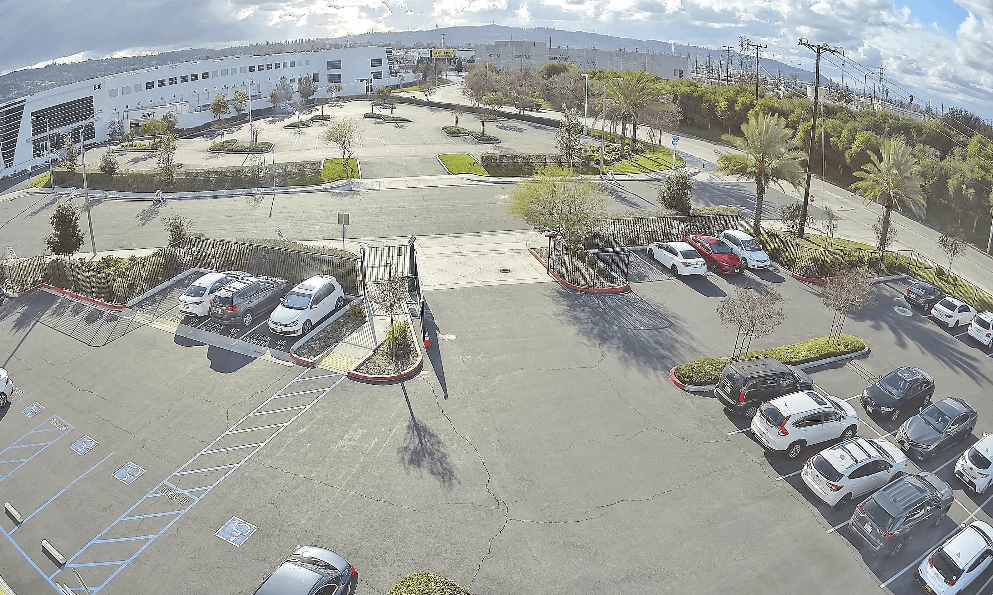 Witness a vast, sunlit parking lot captured through the lens of a panoramic security camera, showcasing an array of vehicles and the impressive expanse of organized asphalt.